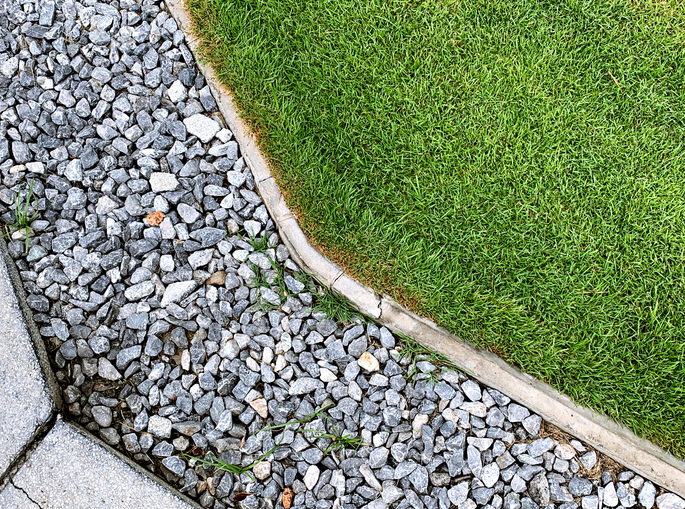 Practical use of drain rock in landscaping around a green lawn.