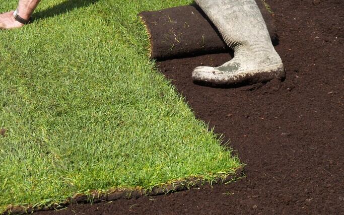Worker leveling topsoil on a lawn, illustrating how much topsoil do I need for landscaping.