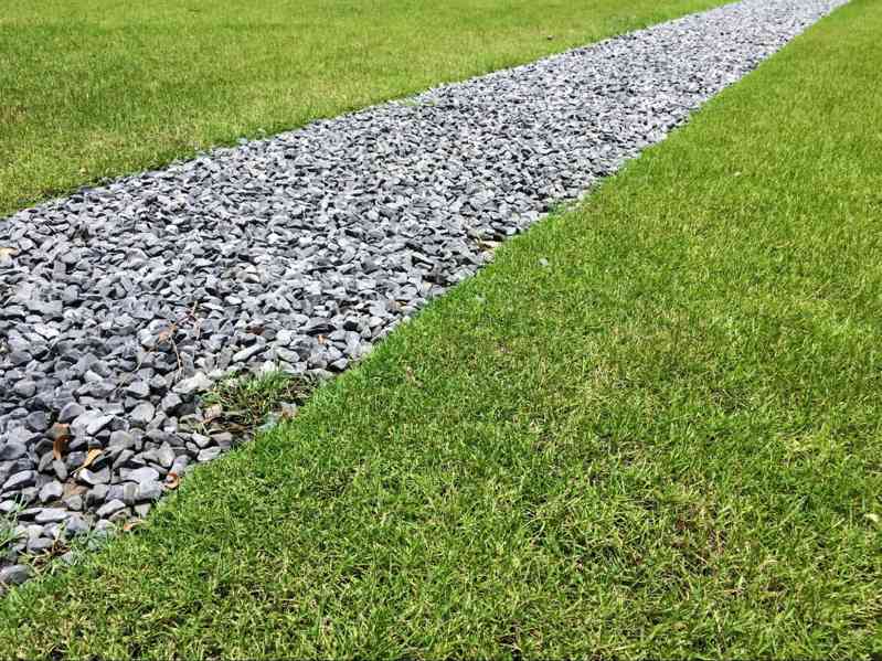Drain rock installed in a landscaped drainage channel to improve water runoff, erosion control, and residential yard drainage performance.
