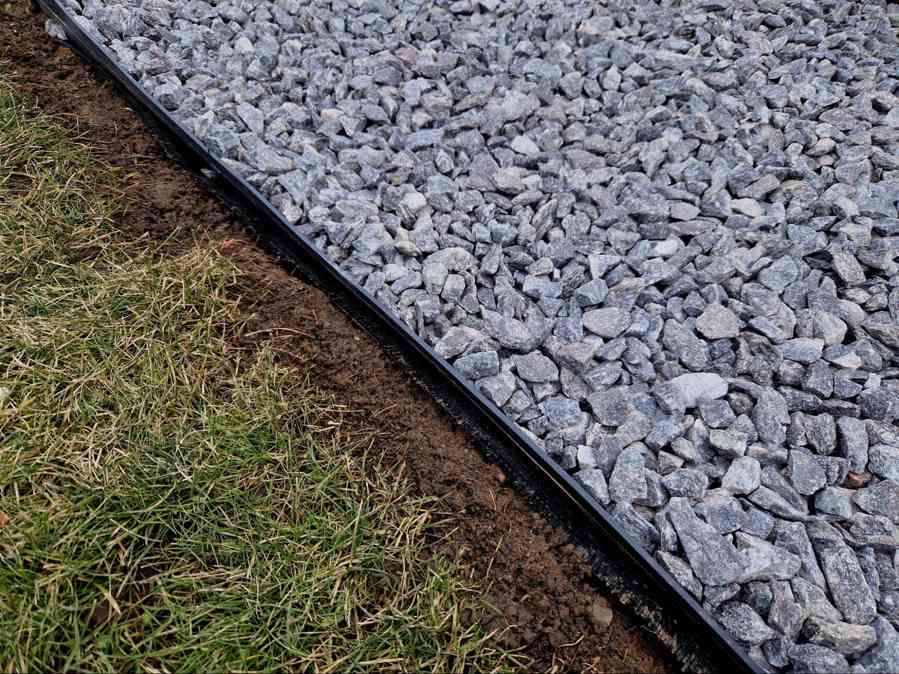 Close-up of drain rock installed beside lawn edging for landscape drainage, water management, and erosion control around residential property.