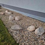 Washed rock landscaping installed along residential home foundation for drainage, erosion control, and clean decorative curb appeal.