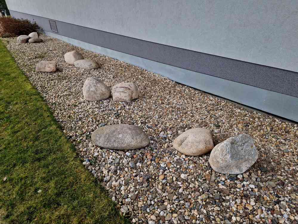 Washed rock landscaping installed along residential home foundation for drainage, erosion control, and clean decorative curb appeal.