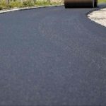 Recycled asphalt driveway surface being compacted with a roller, showing a smooth paved area made from reused asphalt material.
