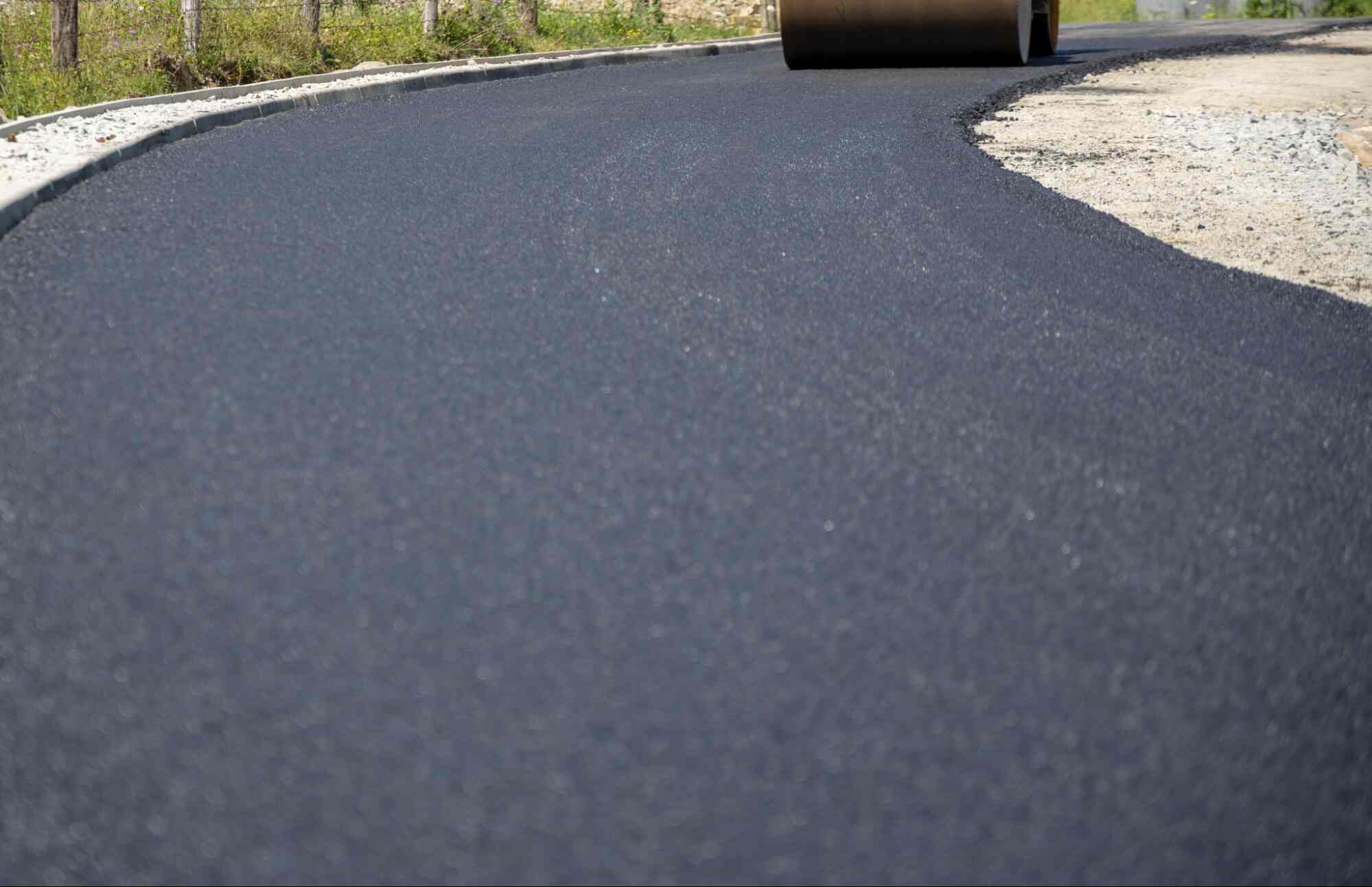 Recycled asphalt driveway surface being compacted with a roller, showing a smooth paved area made from reused asphalt material.