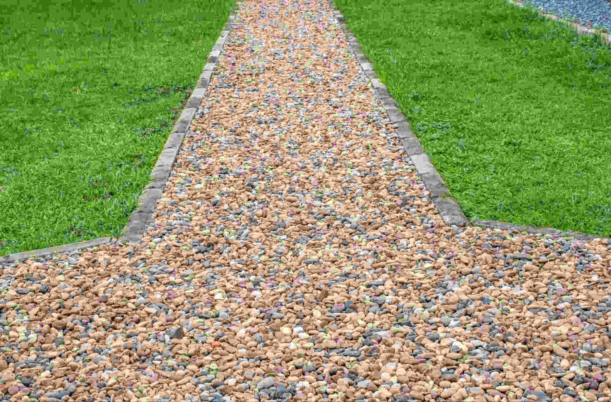 Tan rock landscaping pathway surrounded by green grass, showcasing decorative gravel used for walkways and outdoor landscape design.