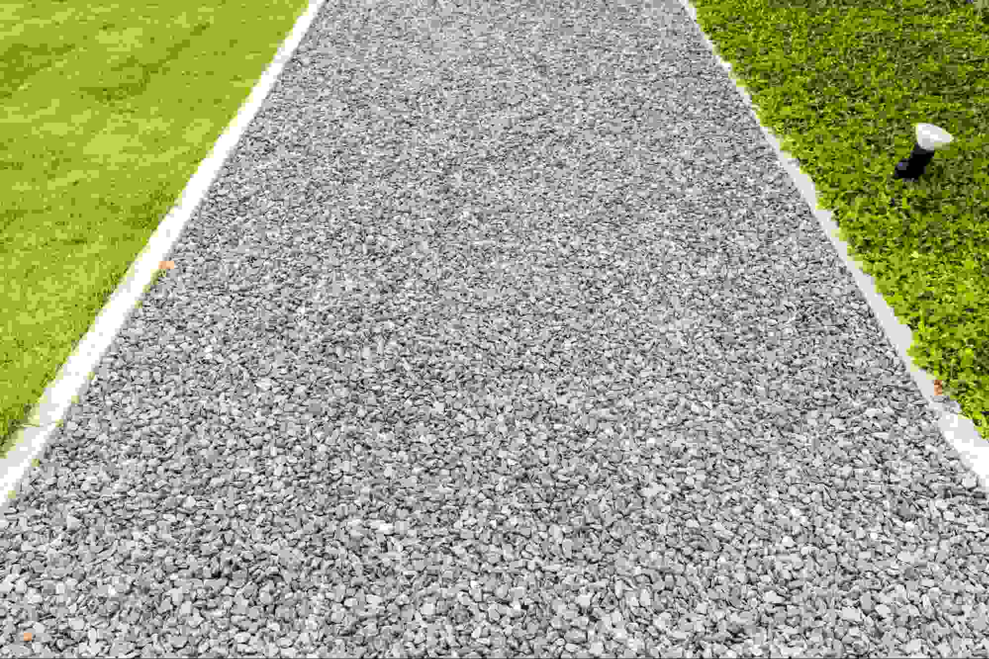 Gravel pathway made with crushed road gravel bordered by green grass, demonstrating what road gravel is used for in walkways, landscaping, drainage, and durable outdoor surfaces.