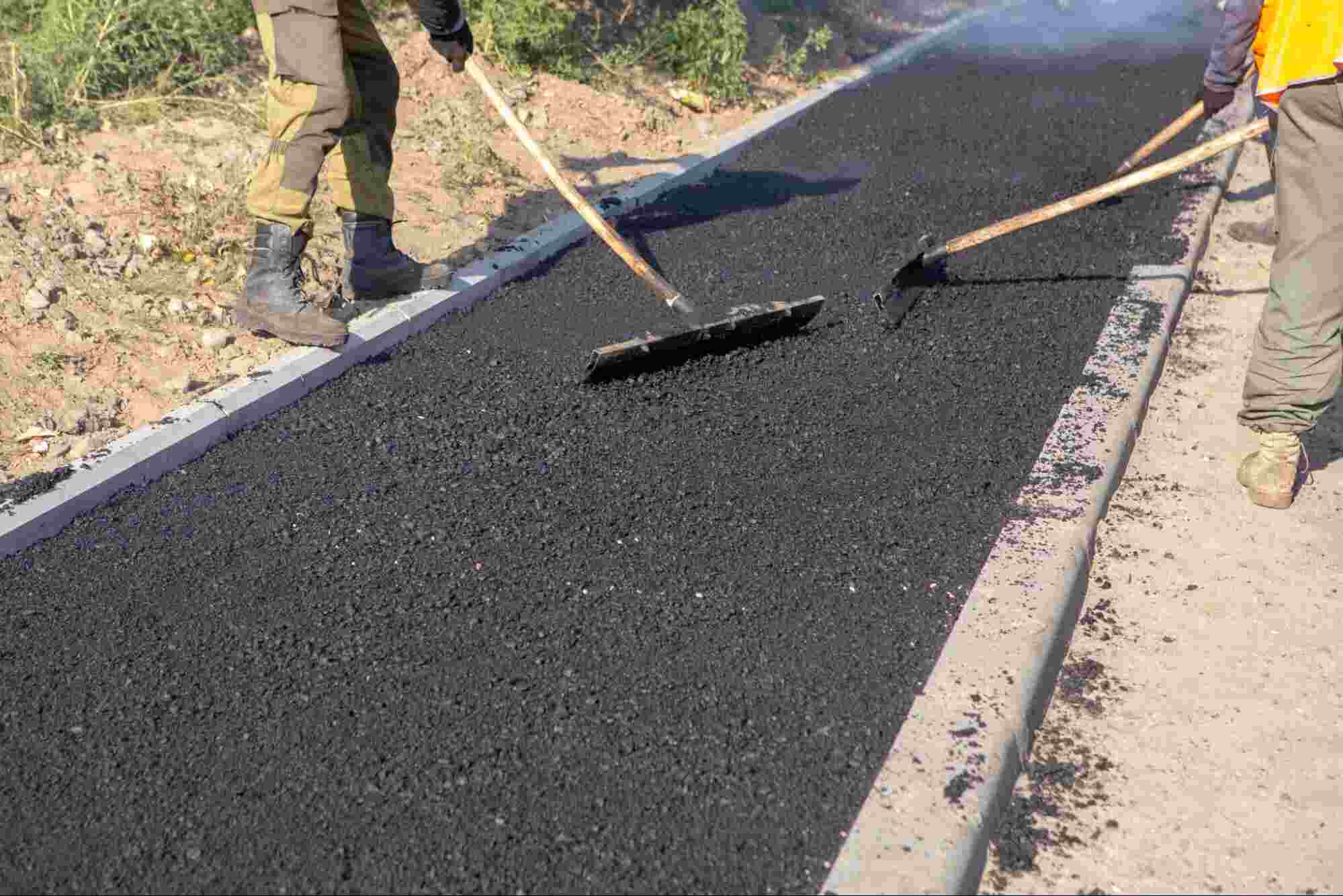 Workers installing recycled asphalt driveway material, showing a newly applied asphalt surface made from reclaimed pavement materials.