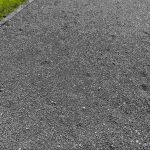 Close-up of a compacted gravel road surface bordered by grass, illustrating what road gravel looks like and how it provides a durable base for pathways and road construction.