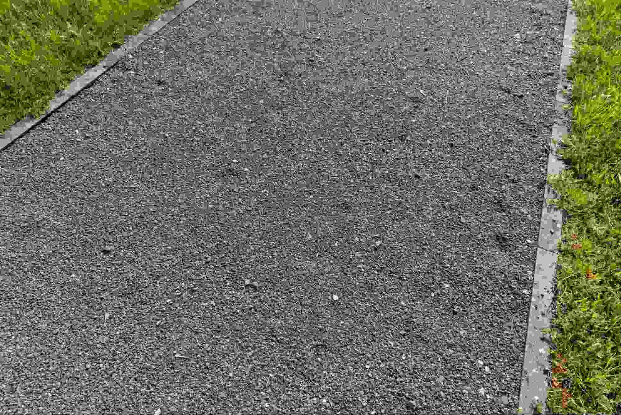 Close-up of a compacted gravel road surface bordered by grass, illustrating what road gravel looks like and how it provides a durable base for pathways and road construction.