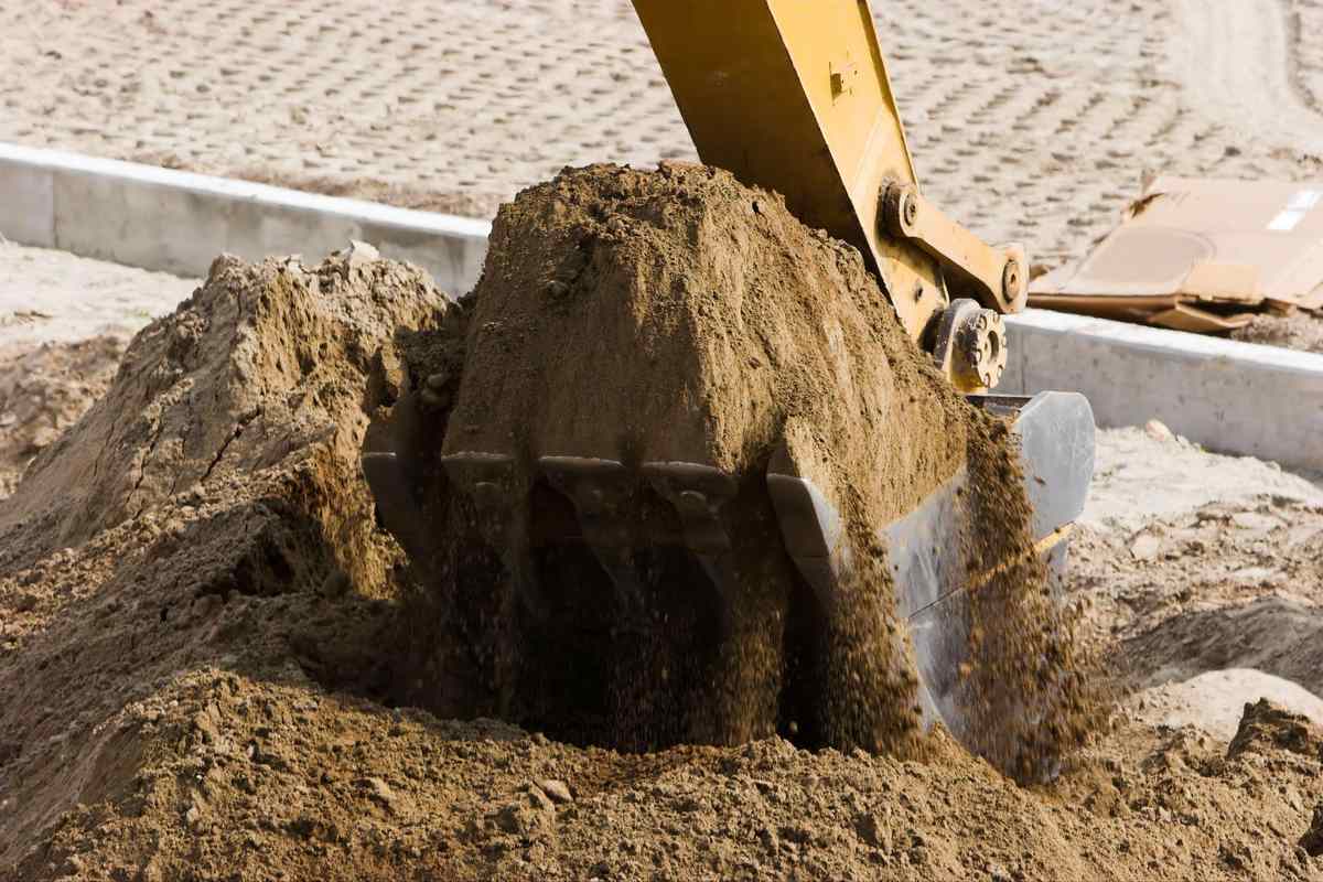 Excavator digging and moving clay soil at a construction site during foundation and site preparation work.