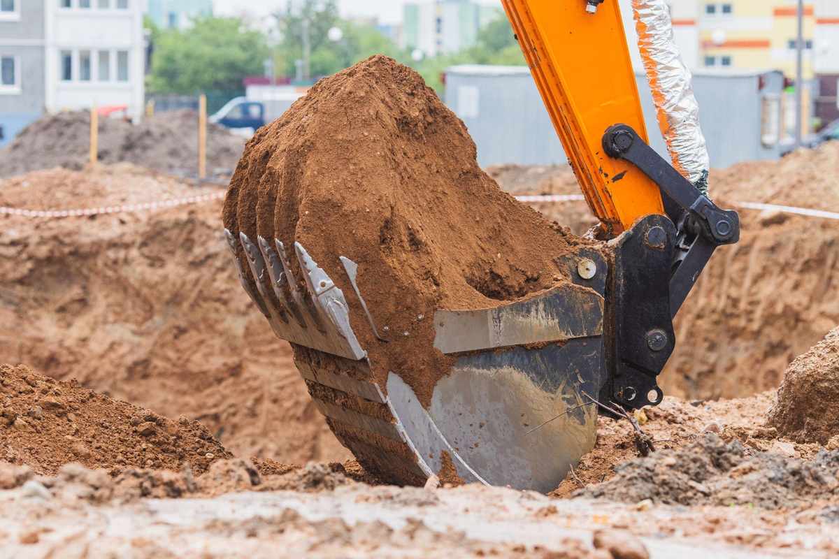 Excavator digging and moving clay soil at a construction site during foundation and site preparation work.